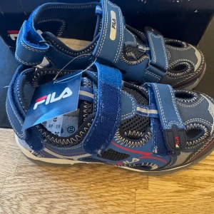 Blå sandaler från Fila - Snygga blå sandaler från Fila med justerbara kardborreband och ventilerande meshdetaljer. Perfekta för sommarens äventyr med en bekväm passform och slitstark sula.