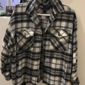 Rutig skjortjacka från Zara - Säljer en snygg rutig skjortjacka från Zara i svart, grått och vitt. Jackan har långa ärmar och knappar framtill. Perfekt för lager-på-lager-stilen och ger en avslappnad look.