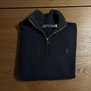 Svart tröja med dragkedja från Ralph Lauren - Säljer en stilren svart tröja från Ralph Lauren med dragkedja vid halsen. Tröjan har långa ärmar och en liten broderad logga på bröstet. Perfekt för en klassisk och avslappnad look. Hör bara av dig vid någon fråga.