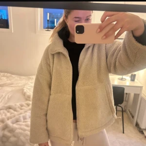 Beige teddyjacka med dragkedja - Mysig beige teddyjacka från carin wester med dragkedja framtill. Perfekt för kyliga dagar med sin fluffiga och varma design. Jackan har en avslappnad passform och långa ärmar.