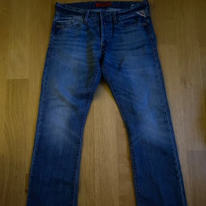 Blå jeans från Replay - Snygga blå low waist jeans från Replay med klassisk femficksdesign och knappgylf. De har en lätt tvättad look och är perfekta för en avslappnad stil. Märkesdetaljer syns på bakfickan och linningen.