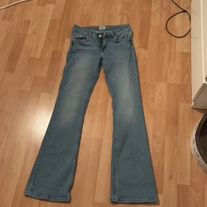 Ljusblå bootcut jeans - Snygga ljusblå lågmidjade bootcut jeans med klassisk femficksdesign och knappgylf. Perfekta för en avslappnad stil med en touch av retro. Passar bra till både sneakers och klackar. Nypris 400kr
