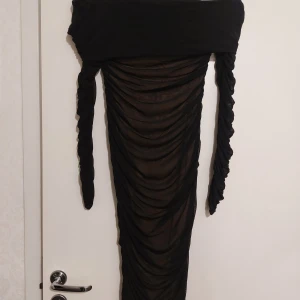 Svart offshoulder klänning - Snygg svart offshoulder klänning med transparenta detaljer och rynkad design. Klänningen har långa ärmar och en figurnära passform som ger en elegant look. Perfekt för en kväll ute eller en speciell tillställning.