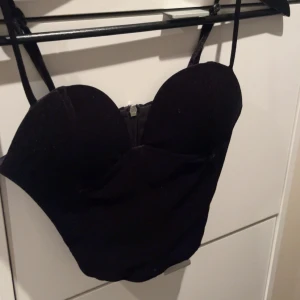 Svart korsett med dragkedja - Snygg svart korsett med dragkedja bak och smala axelband. Perfekt för en stilren look.