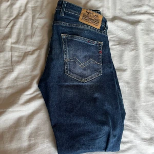 Blå jeans från Replay - Snygga blå jeans från Replay med klassisk femficksdesign och en liten logga vid fickan. De har en bekväm passform och är perfekta för en avslappnad stil. Jeansens mörkblå färg ger en tidlös look. Storlek W 30 L32 
