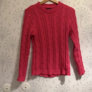 Rosa stickad tröja - Säljer en snygg rosa stickad tröja med kabelstickat mönster. Tröjan har långa ärmar och en rund halsringning. Perfekt för kyligare dagar och ger en mysig känsla. Passar bra till jeans eller kjol för en avslappnad look.