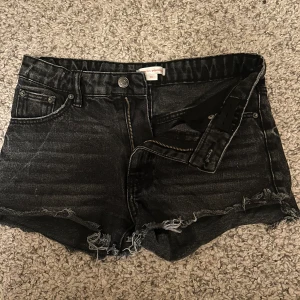 Svarta jeansshorts från Gina Tricot - Snygga svarta lågmidjade  jeansshorts från Gina Tricot med fransiga kanter och dragkedja. Perfekta för en avslappnad stil. De har en klassisk femficksdesign och knappstängning.