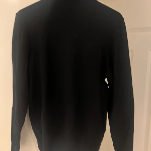 Svart polotröja från Zara - Säljer en stilren svart polotröja från Zara. Perfekt för kyligare dagar med sin klassiska design och bekväma passform. Tröjan har långa ärmar och är tillverkad i ett mjukt material. Tröjan sitter mycket bättre än vad det verkar som på bilden. Den är väldigt slim.