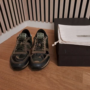 Valentino Rockrunner i camouflage - Säljer ett par snygga Valentino Rockrunner sneakers i camouflage. De har en cool mix av gröna och bruna nyanser med svarta detaljer. Skorna är i mocka och skinn, och har den klassiska rockstud-detaljen på hälen. Perfekta för att ge din outfit en edgy touch!