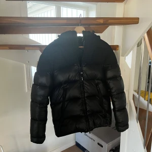 Svart pufferjacka från Replay - Säljer en snygg svart pufferjacka från Replay. Den är perfekt för kalla dagar med sitt tjocka vadderade material. Jackan har en dragkedja framtill och långa ärmar. Den är i mycket bra skick och passar perfekt för höst och vinter. Perfekt för dig som vill hålla stilen i kylan!