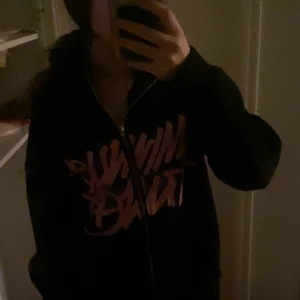 Svart hoodie med rosa tryck - Säljer en svart hoodie med coolt rosa tryck på framsidan. Den har en dragkedja som går ända till huvudet och är perfekt för en avslappnad stil. Passar bra till både vardag och chillkvällar. Hör av dig om du är intresserad! ❤️