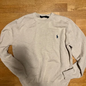 Beige tröja från Polo Ralph Lauren - Säljer en stilren beige tröja från Polo Ralph Lauren i storlek M. Den är stickad och har en klassisk rund halsringning. Tröjan har långa ärmar och den ikoniska loggan broderad på bröstet. Perfekt för både höst och vår!