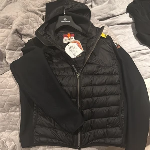 Svart jacka från Parajumpers - Säljer en svart Parajumpers jacka i storlek M. Den har en quiltad design med dragkedja och huva. Perfekt för höst och vår, och den är i nytt skick. Jackan är både stilren och funktionell, idealisk för vardagsbruk.