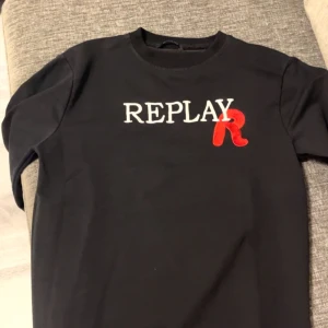 Svart tröja från Replay - Säljer en snygg svart tröja från Replay i storlek M. Den har en cool vit och röd logga på bröstet. Perfekt för vardagsbruk eller en avslappnad utekväll. Tröjan är i bra skick och gjord av mjukt material för extra komfort.