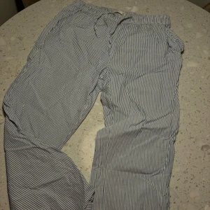 Randiga byxor i blått och vitt - Säljer ett par bekväma randiga pyjamasbyxor i blått och vitt. De har en elastisk midja med snörning för perfekt passform. Perfekta för en avslappnad dag hemma eller en somrig utflykt. 🕶️