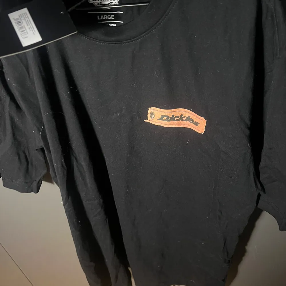 Säljer en svart t-shirt från Dickies i storlek L. Den har ett coolt tryck med olika färgglada etiketter på baksidan och en liten logga på framsidan. Perfekt för vardagsbruk eller avslappnade tillfällen. Helt ny med prislapp kvar!. T-shirts.