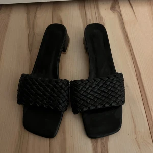 Svarta sandaler med flätad rem - Snygga svarta sandaler med en bred flätad rem över foten. De har en fyrkantig tå och en låg klack, vilket gör dem både stiliga och bekväma. Perfekta för sommarens alla tillfällen! Storleken 40, passar bäst 39. Inte fri frakt.