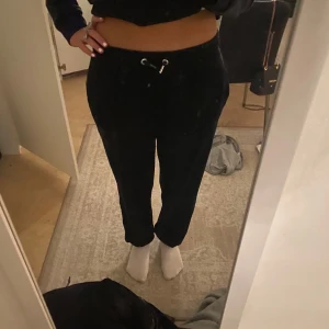 Svarta mjukisbyxor från Juicy Couture - Säljer ett par svarta mjukisbyxor från Juicy Couture i storlek 14/15. Byxorna är supermjuka och bekväma,  ett problem är att en metall del av de snörena är borst vilket man ser på sista bilden men annars är de i bra skick!