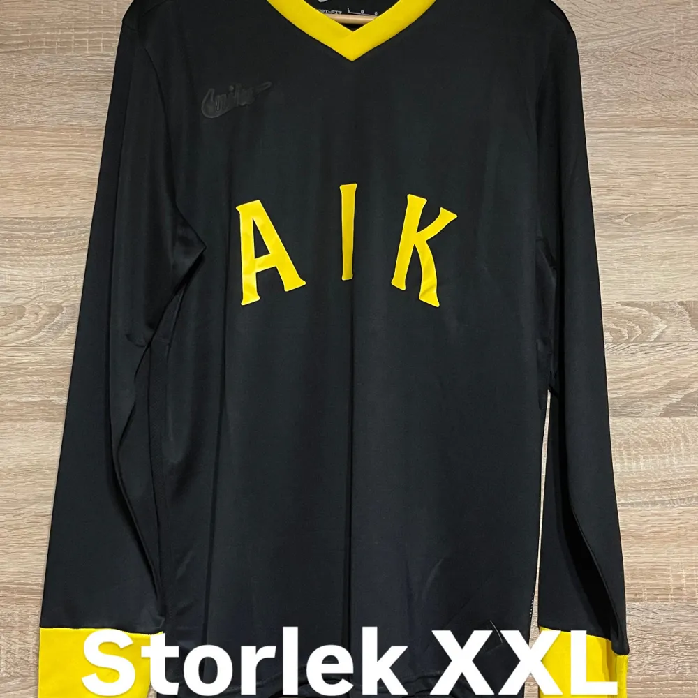 Säljer en svart långärmad AIK-tröja från Nike i storlek XXL. Tröjan har gula detaljer och texten 'AIK' på framsidan. Perfekt för fans som vill visa sitt stöd med stil. Tröjan är i mycket bra skick och har en snygg design med klubbens emblem från 1924.. T-shirts.