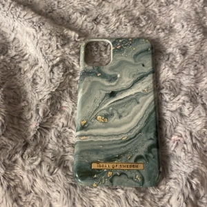Mobilskal från Ideal of Sweden - Snyggt mobilskal från Ideal of Sweden med ett marmorliknande mönster i gröna och guldiga toner. Skalet har en lyxig känsla och passar perfekt för att ge din mobil en stilfull look. Det är i bra skick och redo att användas direkt. Perfekt för dig som vill ha en unik och trendig accessoar till din telefon.