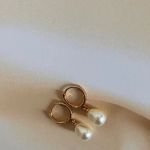 Örhängen med pärldetaljer - Säljer ett par eleganta handgjorda örhängen med vackra pärldetaljer. Perfekta för både vardag och fest! De har en klassisk design med en liten pärla som hänger från en guldring. Passar till alla tillfällen och ger en touch av lyx till din outfit. 🥰 Handgjorda örhängen.