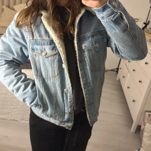 Ljusblå jeansjacka med teddyfoder - Säljer en snygg ljusblå jeansjacka med mysigt vitt teddyfoder. Jackan har en klassisk design med knappar framtill och två bröstfickor. Perfekt för höst och vår när du vill hålla stilen men ändå vara varm. Passar till både vardag och fest!