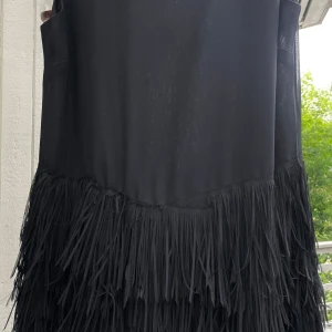 Svart coctaildress, festklänning med fransar - Snyggast på festen, klänning med massor av frasar, kul att dansa i. Dubbelt tyg. Ärmlös.