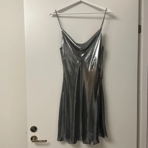 Silverfärgad klänning från Zara - Snygg silverfärgad klänning från Zara i ett glansigt material. Den har smala axelband och en elegant draperad halslinje. Perfekt för festliga tillfällen när du vill glänsa lite extra! ✨tryck gärna på köp nu💕