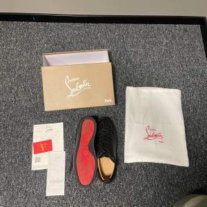 Säljer ett par svarta sneakers från Christian Louboutin i nytt skick. Skorna har en ikonisk röd sula och är dekorerade med nitar på ovansidan. De är gjorda av skinn och har snörning för en perfekt passform. Perfekta för att ge din outfit en edgy touch!äkta💯