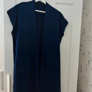 Mörkblå ärmlös väst - Snygg mörkblå ärmlös väst i normal passform. Perfekt för lager-på-lager under höst och vår. Västen har en enkel design med två fickor framtill. Ett mångsidigt plagg som funkar både till vardags och fest.