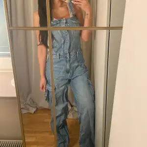 Säljer en snygg jeansbyxdress i blå denim. Den har justerbara axelband och flera fickor, vilket ger en cool och avslappnad look. Perfekt för en casual dag ute eller en avslappnad fest. Passformen är loose och den är i mycket bra skick.