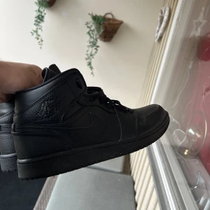 Svarta Nike Air Jordans 1 - Säljer ett par svarta Nike Air Jordans i bra skick. De är helt svarta med snörning och har den klassiska Air Jordan-loggan på sidan. Perfekta för både vardag och fest. Skorna är bekväma och stilrena, passar till det mesta i garderoben.