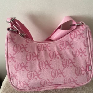 Rosa axelväska med mönster - Säljer en superfin rosa axelväska med en 90’s inspirerad mönster. Väskan har en justerbar axelrem och är perfekt för vardagsbruk. Den är i mycket bra skick och har en snygg design som verkligen sticker ut. Perfekt för att ge lite färg till din outfit!