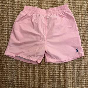 Säljer ett par snygga rosa shorts från Polo Ralph Lauren i storlek L, men passar mer som M. De har en elastisk midja och en liten broderad logga i blått på framsidan. Perfekta för sommardagar vid stranden eller poolen! 🏖️