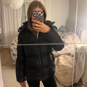 Svart vinterjacka från Tommy Hilfiger  - Säljer en svart dunjacka från Tommy Hilfiger i bra skick. Den har en dragkedja framtill och är perfekt för kalla dagar. Jackan är långärmad och har en mysig, och passar både för tjejer och killar. Perfekt för vintern och hösten! Jackan har en liten liten skrapa på baksidan av ena armen, finns bild att se. Men det är inget man märker av!!