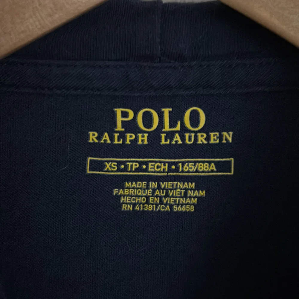 Säljer en stilren mörkblå hoodie från Ralph Lauren i storlek XS. Den har en klassisk design med en liten röd logga på bröstet och justerbara snören i huvan. Perfekt för både vardag och avslappnade tillfällen. Skön och enkel att matcha med det mesta! 💙. Neuletakit & Villapaidat.
