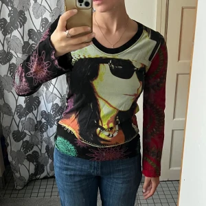 Färgglad långärmad tröja från Desigual - Säljer en unik långärmad tröja från Desigual. Den har ett coolt tryck av en person på framsidan, och mönstrade ärmar i olika färger. Perfekt för dig som vill sticka ut! Tröjan är i bra skick. Det står ingen storlek, men jag skulle säga att den passar till S och M. Jag har sytt in tröjan i båda sidor, då jag tyckte den satt för löst. Om man vill ha den större kan man enkelt sprätta upp sömnen. Köparen står för frakt, skickar spårtbart PostNord paket.