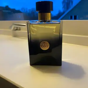 Säljer en elegant flaska Oud Noir Eau de Parfum från Versace. Flaskan har en stilren design med en mörk gradient och en gyllene detalj i mitten. Perfekt för den som vill ha en lyxig och mystisk doft. Flaskan är nästan full och redo att användas. Passar perfekt för speciella tillfällen eller som en fin present.