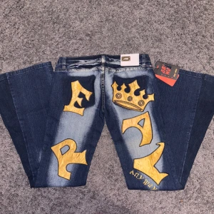 Blå jeans med gul krona och text - Unika blå jeans från Any Way med stora gula applikationer av en krona och text på baksidan. Byxorna är utsydda rill bootcut därmed en extra söm. Innerbenslängd 84 cm och rvärs över midjan är 39 cm ❤️ PRISET ÄR DISKUTERBART!!! ❤️❤️