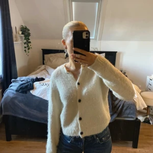 Vit fluffig kofta med knappar - Mysig vit kofta med fluffig textur och svarta knappar. Perfekt för kyligare dagar. Långärmad och i en stilren design som passar till det mesta.