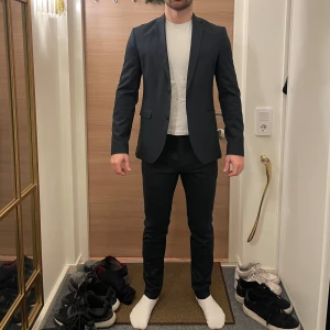 Mörkblå kostym från Premium by Jack & Jones - Snygg mörkblå kostym från Premium by Jack & Jones. Perfekt för en stilren look med två knappar framtill och klassisk passform. Passar utmärkt till både formella och semi-formella tillfällen. Storlek på kavajen: 48 storlek på byxorna: 46