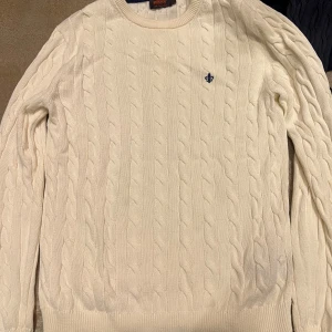 Vit kabelstickad tröja från Morris - Säljer en stilren vit kabelstickad tröja från Morris i 100% Pima bomull. Tröjan har en liten broderad detalj på bröstet och långa ärmar. Perfekt för en klassisk och tidlös look.