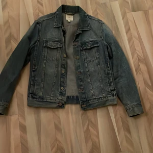 Blå jeansjacka från H&M - Snygg blå jeansjacka från H&M med klassisk design. Jackan har två bröstfickor med knappar och en stilren krage. Perfekt för en avslappnad look.