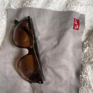 Solglasögon från Ray-Ban - Snygga solglasögon från Ray-Ban med bruna glas och en klassisk svart båge. Perfekta för soliga dagar och kommer med ett stilrent svart fodral. Ett måste för alla som älskar tidlös design.