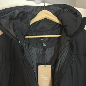 Svart pufferjacka från Vero Moda - Säljer en svart pufferjacka från Vero Moda. Jackan har en lång design med dragkedja och en stor huva för extra värme. Perfekt för kalla dagar.