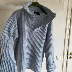 Ljusblå ribbad tröja från Pieces - Säljer en ljusblå ribbad tröja från Pieces med dragkedja vid halsen. Tröjan har långa ärmar och en hög krage som ger en mysig känsla. Perfekt för kyligare dagar!