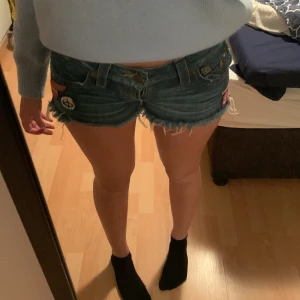 Jeansshorts med patches från True Religion - Säljer ett par coola jeansshorts från True Religion med flera patches och slitna detaljer. Perfekta för en avslappnad stil med låg midja och fransiga kanter. Passar perfekt för sommardagar! Säljer dessa då de sitter lite för tajt på mig, använd 1 gång.