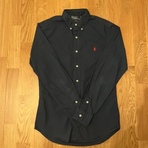 Blå Ralph Lauren skjorta - Säljer nu denna snygga Ralph Lauren skjortan i färgen marinblå och storlek S. den passar bra mellan 165-170. Självklart äkta och den är i nyskick. Nypris på denna är runt 1000kr. Om ni undrar något, tveka inte att fråga så är jag snabb med att ge svar. PRIS KAN DISKUTERAS 