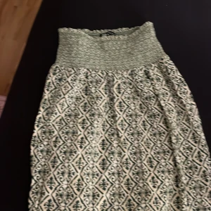 Mönstrad långkjol i grönt och beige - Snygg långkjol med ett unikt mönster i grönt och beige. Kjolen har en bred, elastisk midja som ger en bekväm passform. Perfekt för en bohemisk stil.