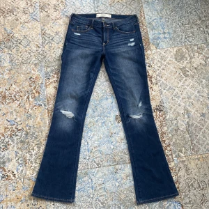 Blå bootcut jeans från Abercrombie & Fitch - Snygga blå bootcut jeans från Abercrombie & Fitch med slitna detaljer på framsidan. De har Inga defekter och är midrise. Midjemått:39cm rakt över. innerbenslängd: ca 78 cm